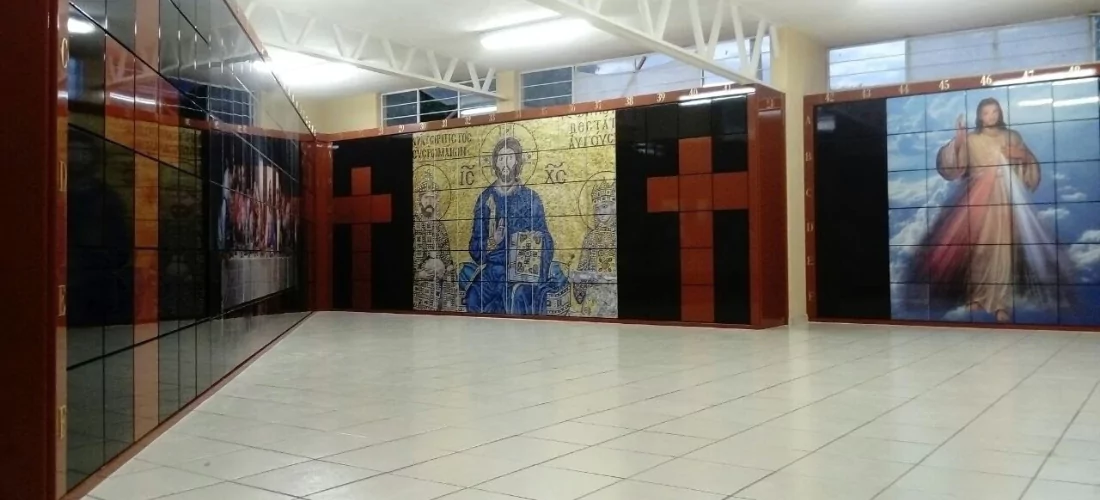 Criptas Salón amplio con murales de mosaico, incluyendo cruces en mármol rojo, una imagen central de Cristo en estilo iconográfico y otra imagen de Jesús a la derecha