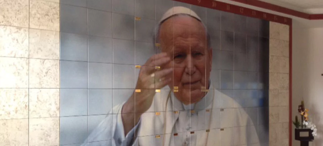 Criptas Muro de nichos con imagen de San Juan Pablo II, en mármol beige con detalles en rojo, creando un espacio solemne y significativo