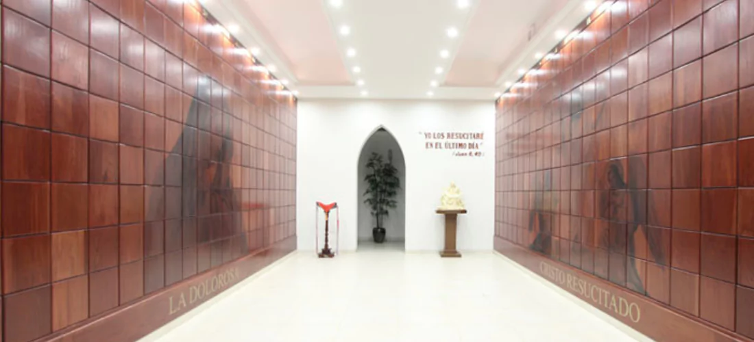 Criptas Pasillo de nichos con imágenes de La Dolorosa y Cristo Resucitado, creando un espacio de reflexión y esperanza. Inscripción: 'Yo los resucitaré en el último día' - Juan 6:40.
