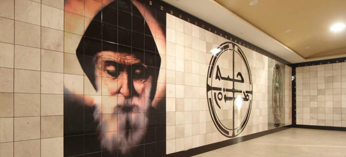 Criptas Muro de nichos decorado con la imagen de San Charbel, un símbolo central religioso y la Virgen de Guadalupe al fondo, creando un espacio de devoción y recogimiento.