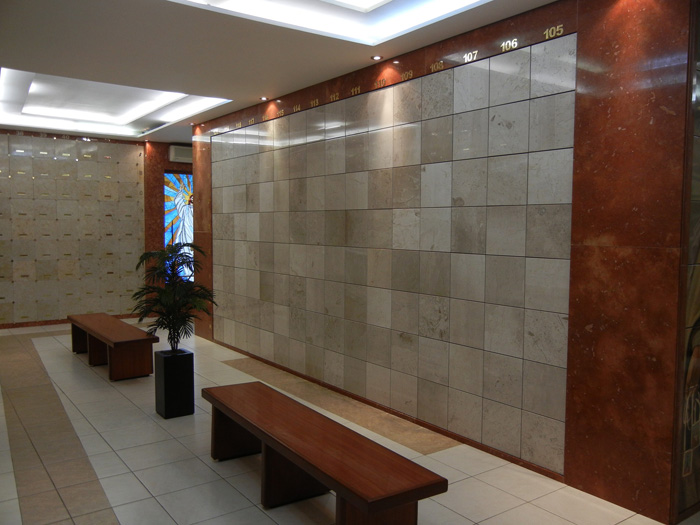 Criptas Pared de nichos de mármol numerados con bancos de madera y una vidriera al fondo.