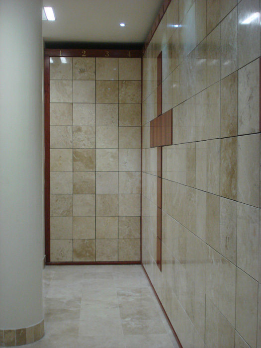 Criptas Muro de nichos en mármol claro, con una cruz formada por baldosas en tonos más oscuros, creando un diseño sutil y elegante en el pasillo.
