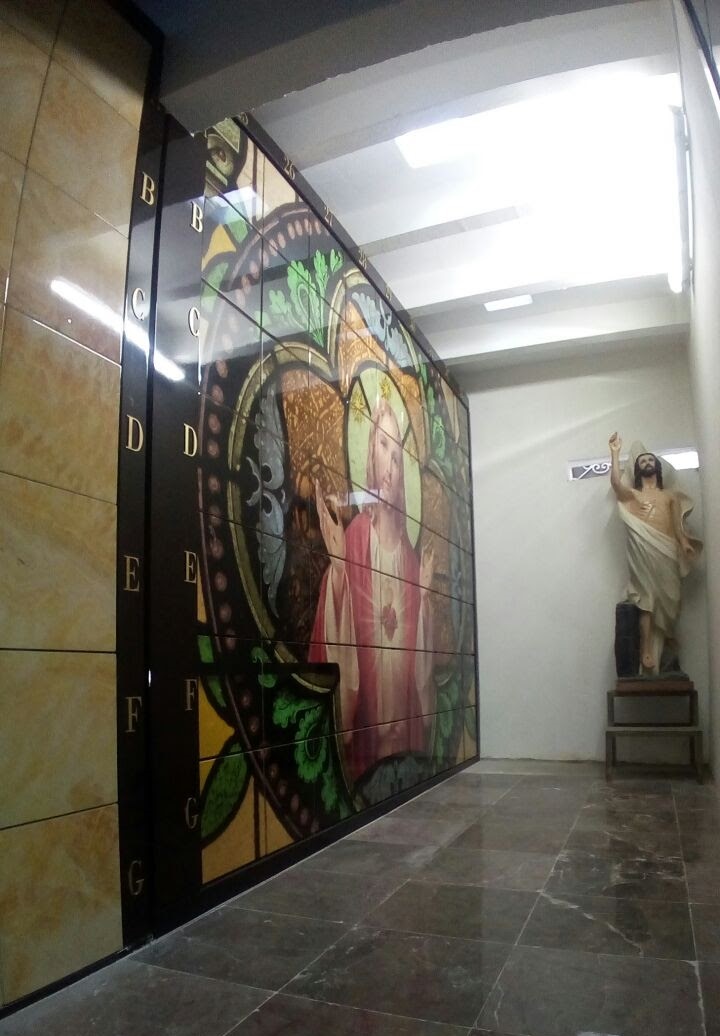 Criptas Mural en mosaico con una imagen de Jesús en estilo de vitral, acompañado de una estatua de Cristo Resucitado en el fondo, con numeración en el borde