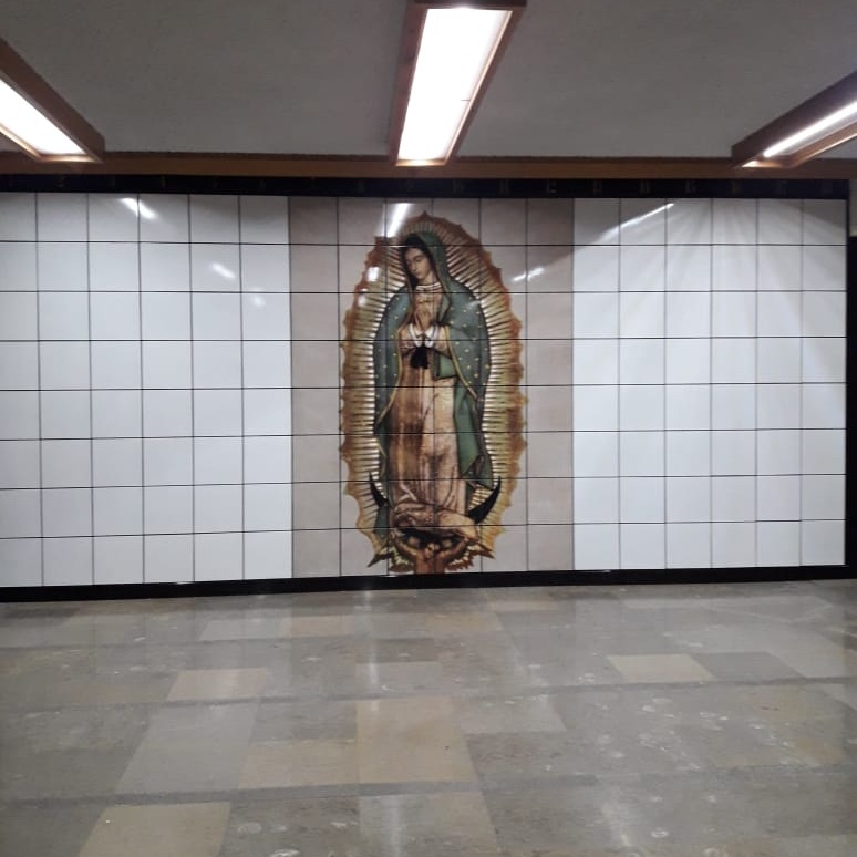 Criptas Mural en mosaico de la Virgen de Guadalupe en el centro de una pared blanca con numeración en el borde superior