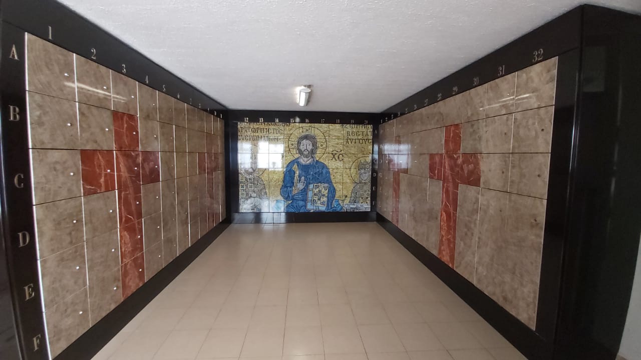 Criptas Pasillo con paredes de mosaico decoradas con cruces en mármol rojo y un mural religioso al fondo que representa a Cristo